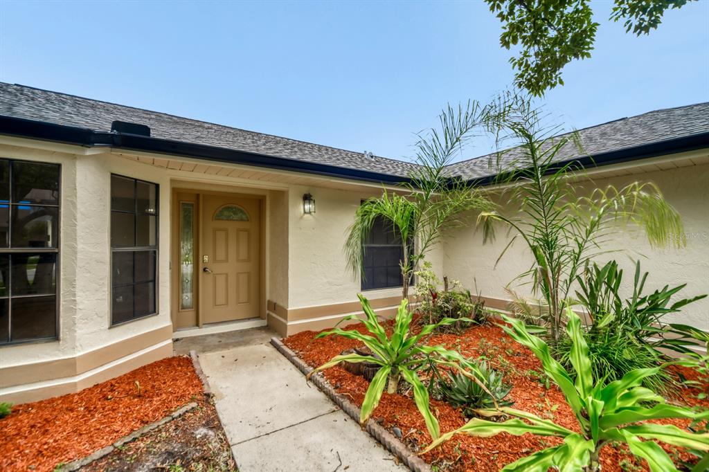 A beige house exterior features a front door, a concrete walkway, and a landscaped garden — 2627 TALON COURT, ORLANDO, FL