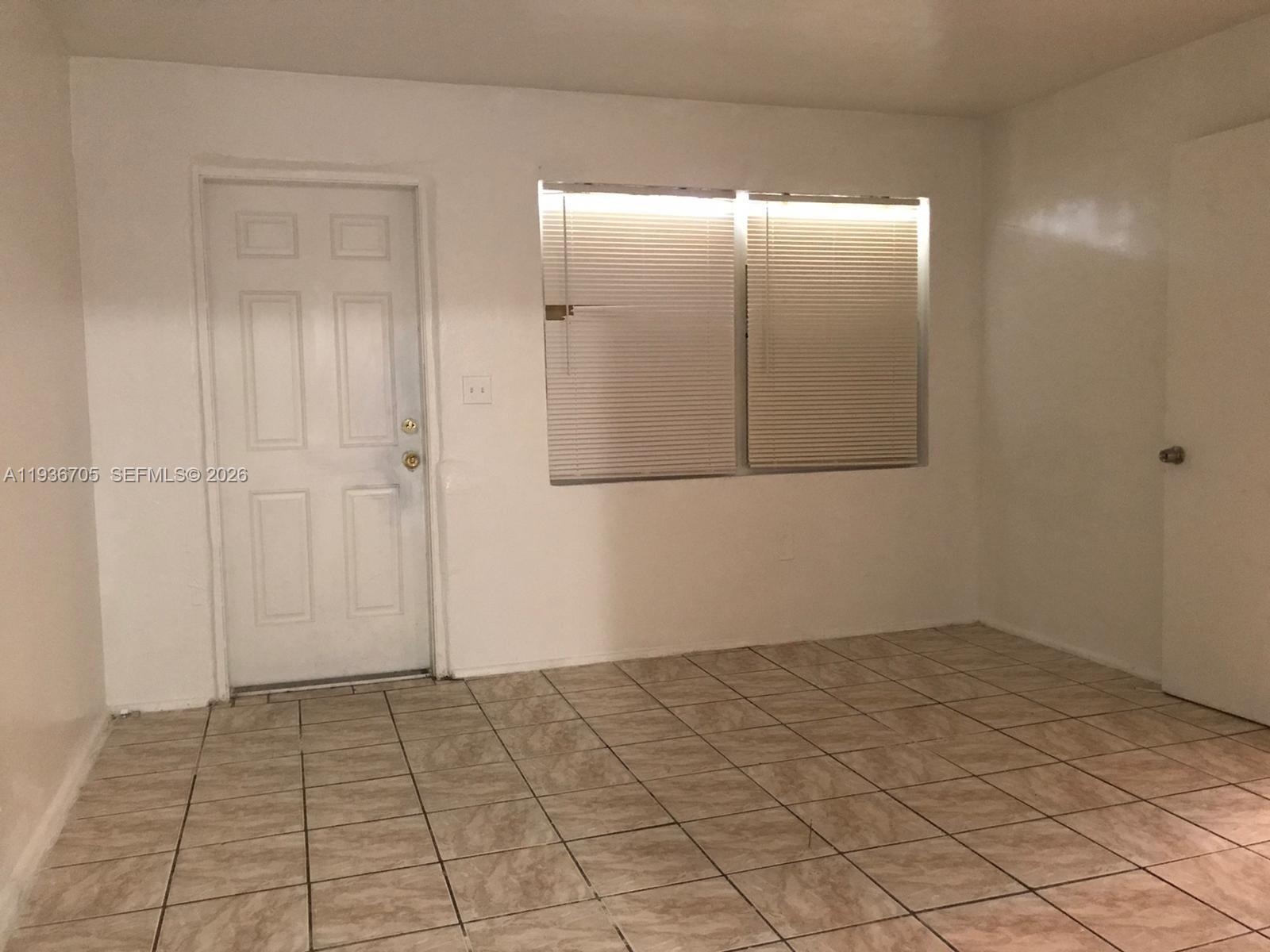 An empty room features white walls, tiled flooring, a white door, and a window with blinds — 1948 NW 2nd Ct # 5, Miami FL 33136, MIAMI, FL