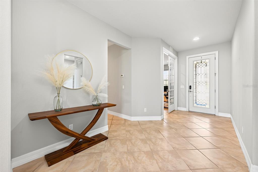 An entryway features a wooden console table, a round mirror, and tile flooring — 17590 SAILFIN DRIVE, ORLANDO, FL
