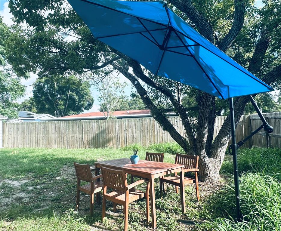 A wooden patio table and chairs sit under a blue umbrella in a grassy backyard — 4716 W WISCONSIN AVENUE, TAMPA, FL