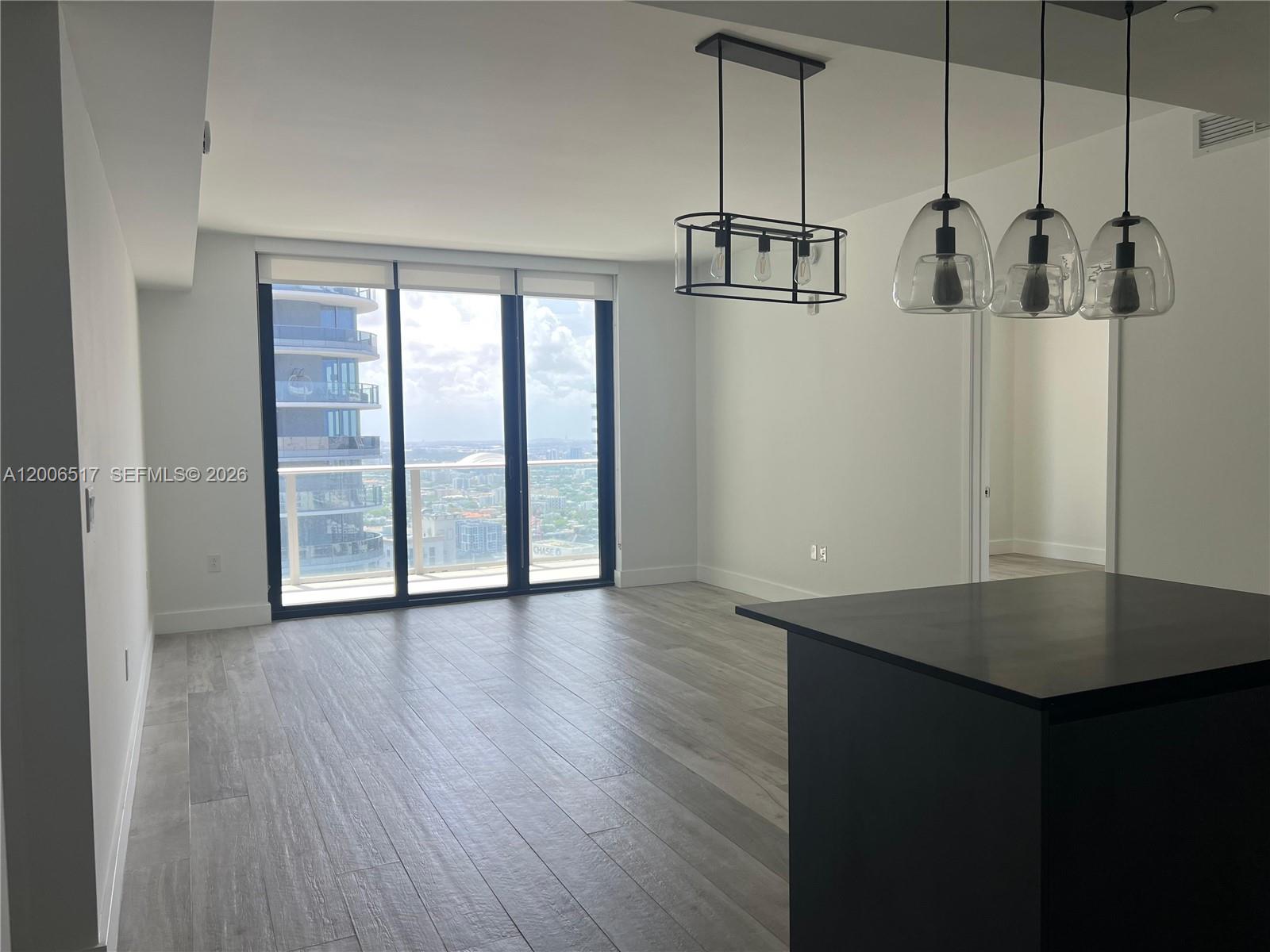 An open-concept living area features light wood-look flooring, modern pendant lighting, and floor-to-ceiling windows — 1010 Brickell Ave # 4609, Miami FL 33131, MIAMI, FL