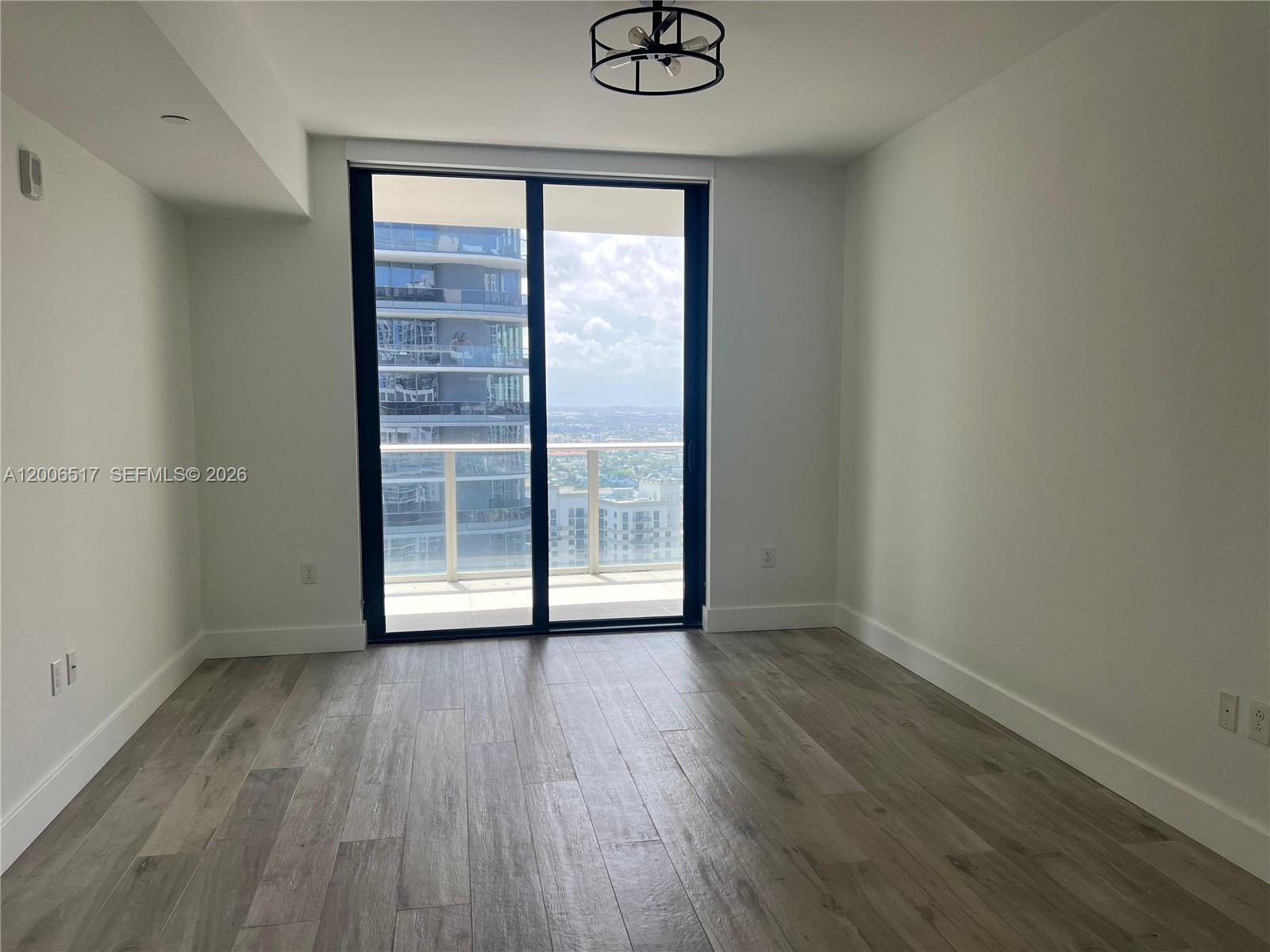 An empty room features light wood-look flooring, white walls, a ceiling light, and a sliding glass door — 1010 Brickell Ave # 4609, Miami FL 33131, MIAMI, FL