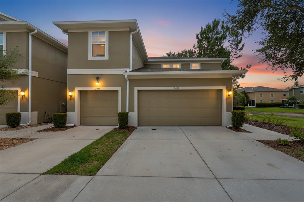 A two-story tan townhouse with two garage doors and a concrete driveway at sunset — 3019 OLD FULTON PLACE, BRANDON, FL