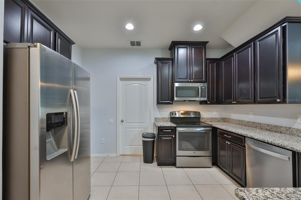 A kitchen features dark wood cabinets, stainless steel appliances, and granite countertops over tile flooring — 3019 OLD FULTON PLACE, BRANDON, FL