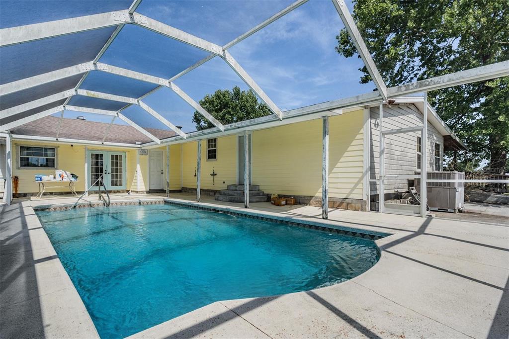 A swimming pool enclosed by a screened lanai sits beside a yellow house with siding — 6606 GATOR RANCH STREET, PLANT CITY, FL