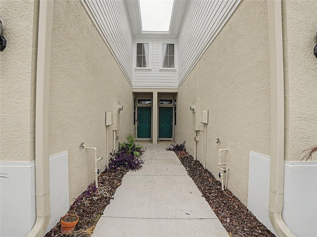 A narrow concrete walkway leads to two green front doors between beige stucco walls — 10942 VERAWOOD DRIVE, RIVERVIEW, FL