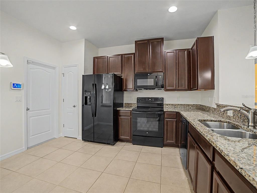 A kitchen features dark wood cabinets, granite countertops, black appliances, and light tile flooring — 10942 VERAWOOD DRIVE, RIVERVIEW, FL