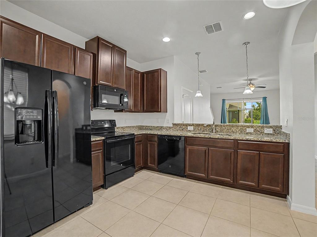 A kitchen features dark wood cabinets, granite countertops, black appliances, and light-colored tile flooring — 10942 VERAWOOD DRIVE, RIVERVIEW, FL