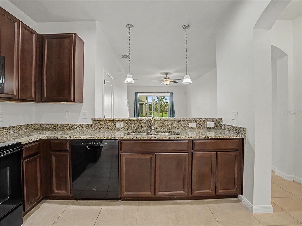 A kitchen features dark wood cabinets, granite countertops, a black dishwasher, and two pendant lights — 10942 VERAWOOD DRIVE, RIVERVIEW, FL