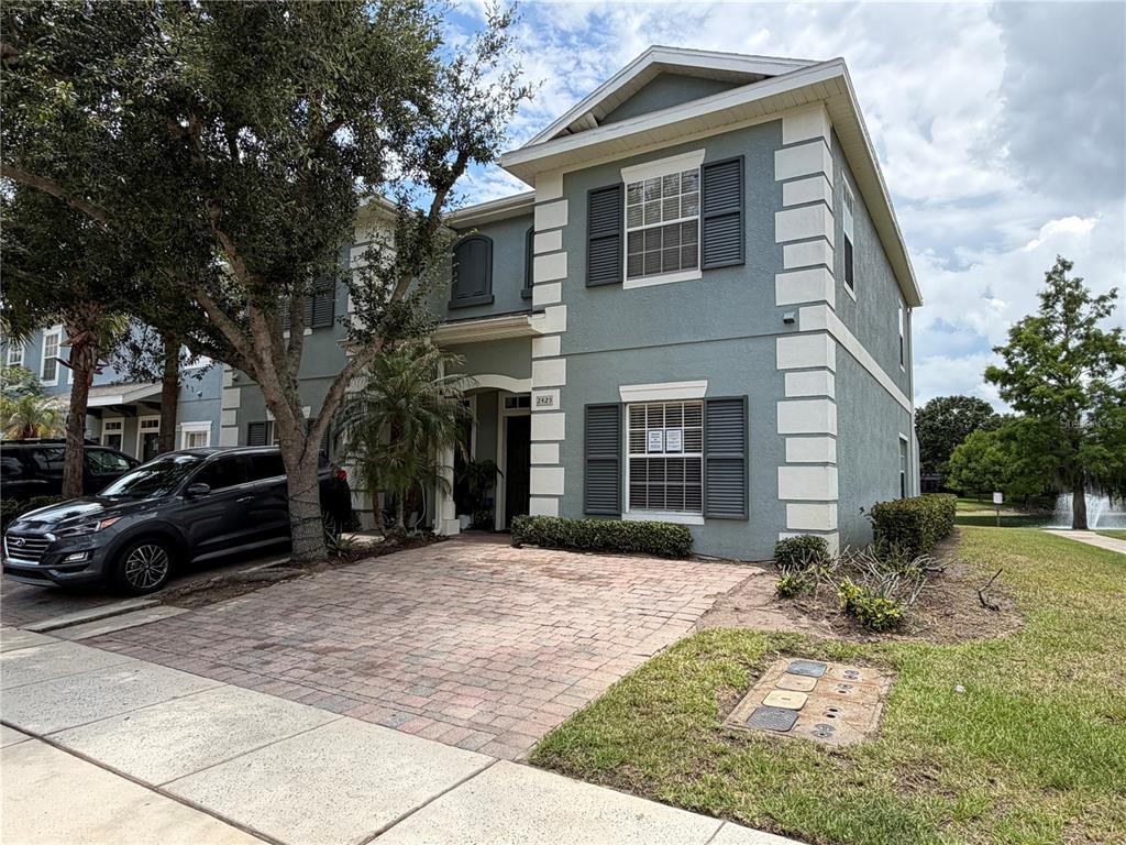 A two-story house with a brick driveway, blue-grey stucco siding, and white corner quoins — 2425 CARAVELLE CIRCLE, KISSIMMEE, FL