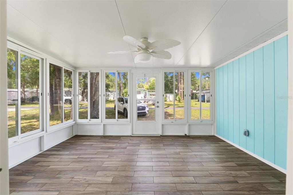 A sunroom features wood-look tile flooring, a white ceiling fan, and light blue paneled walls — 2092 CULBREATH ROAD UNIT C52, BROOKSVILLE, FL