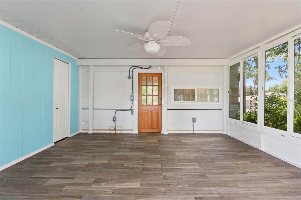 A sunroom features wood-look tile flooring, a ceiling fan, a blue wall, and a wooden door — 2092 CULBREATH ROAD UNIT C52, BROOKSVILLE, FL