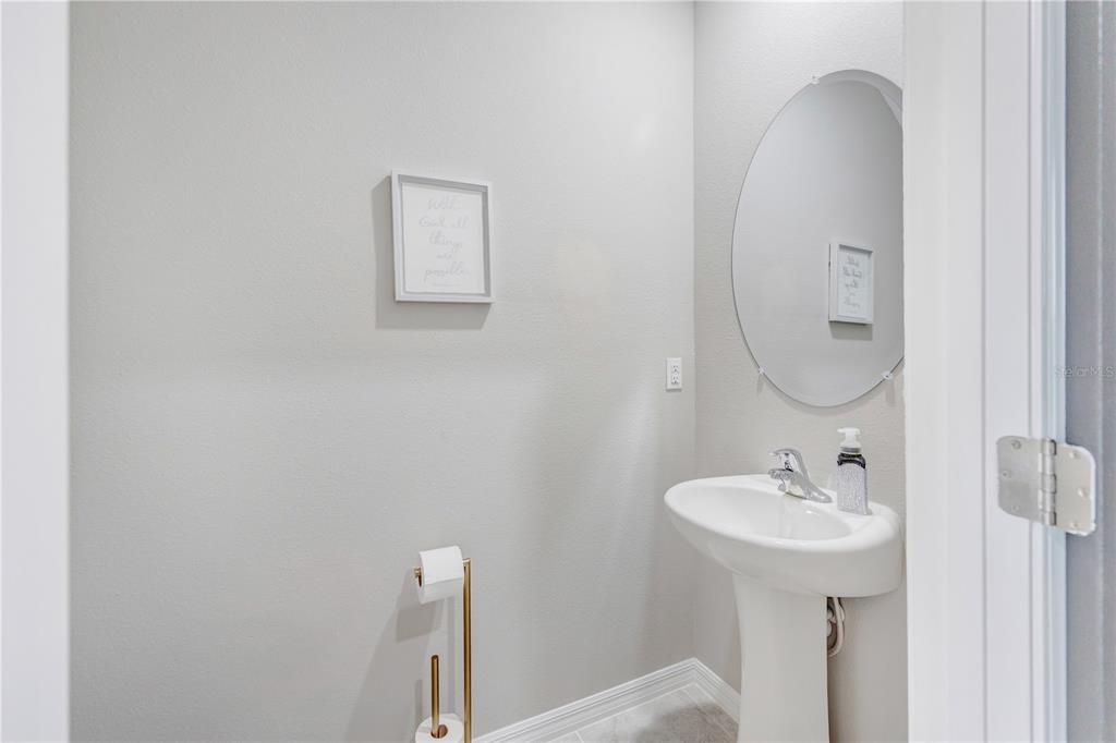 A small powder room features a white pedestal sink, a round mirror, and neutral walls — 5522 APPLETON SHORE DRIVE, APOLLO BEACH, FL