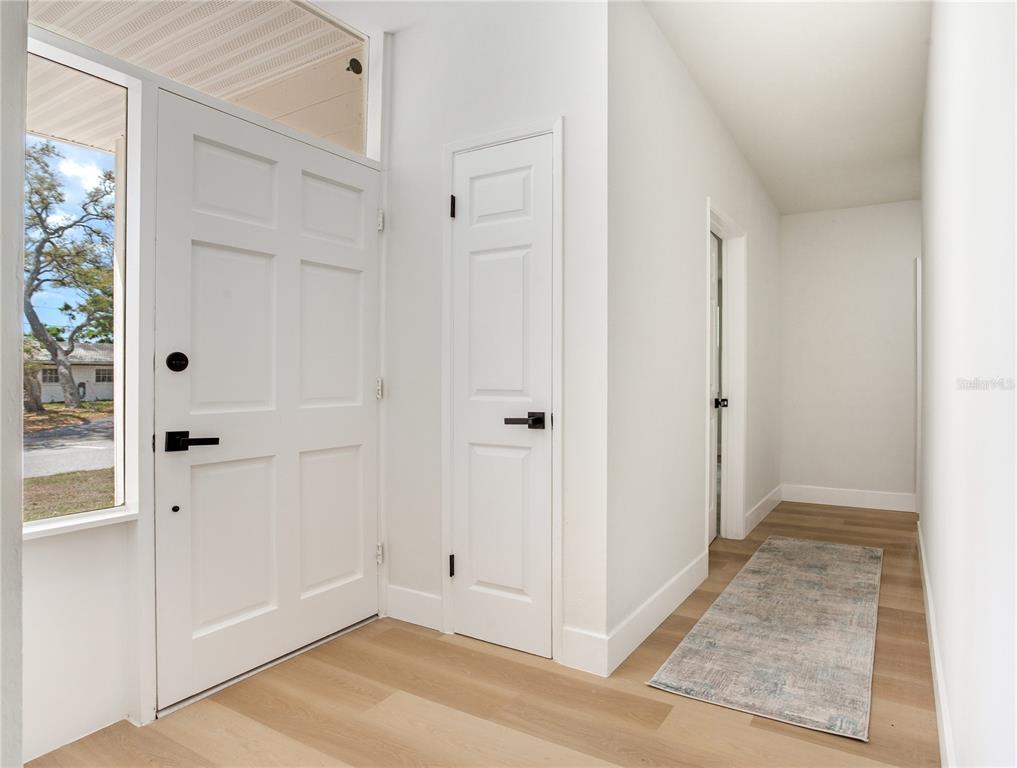 A white front door opens into an entryway with light wood flooring and an adjacent room — 2753 VALENCIA DRIVE, SARASOTA, FL