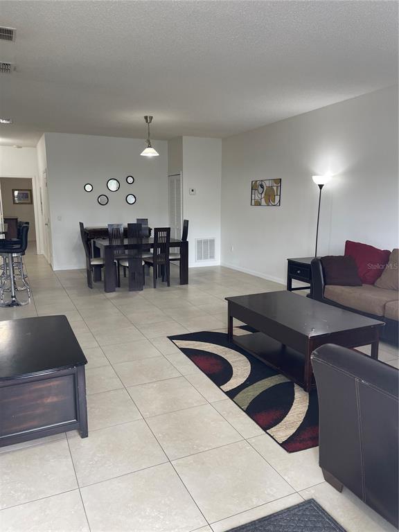 An open-concept living and dining area features tile flooring, dark furniture, and a patterned rug — 3157 SUN LAKE COURT UNIT A, KISSIMMEE, FL