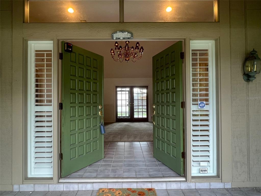An open set of green double doors leads into a tiled foyer with a chandelier — 6328 N QUEENSWAY DRIVE, TEMPLE TERRACE, FL