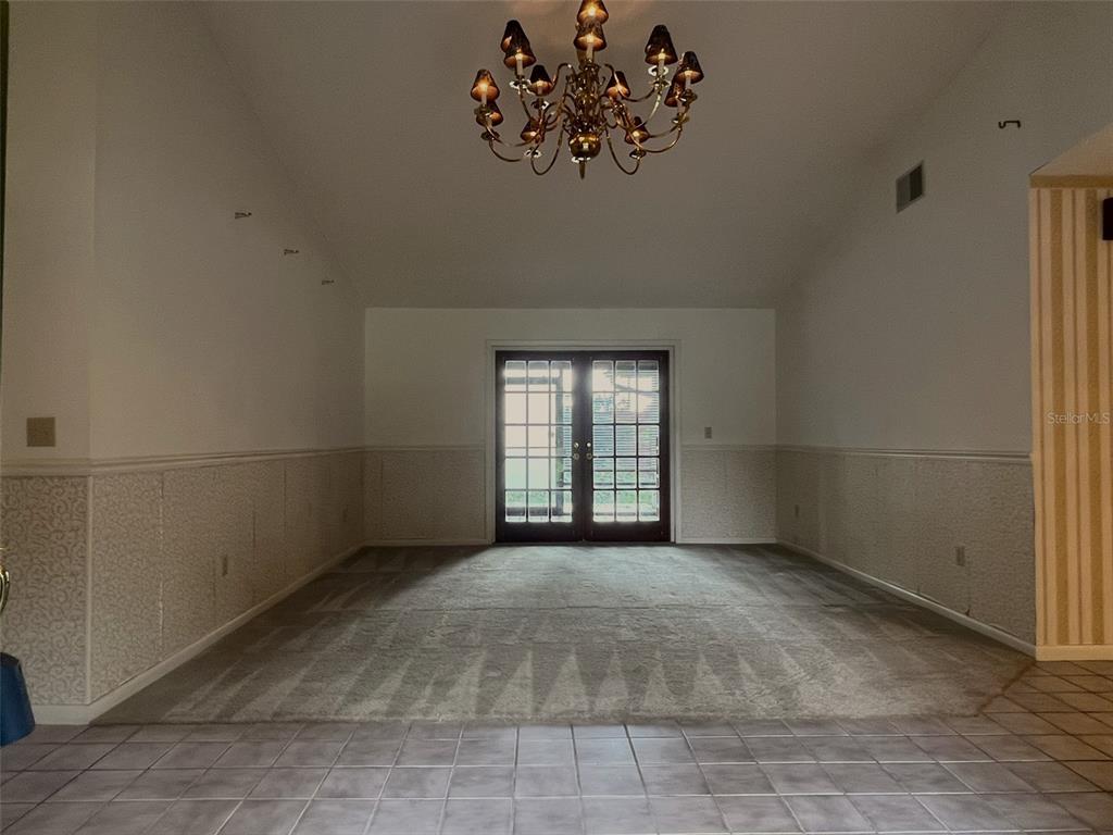A dining room features a chandelier, carpeted flooring, wainscoting, and French doors leading outside — 6328 N QUEENSWAY DRIVE, TEMPLE TERRACE, FL