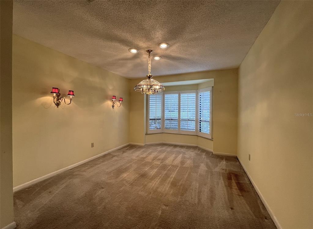 A dining room features beige walls, carpeted flooring, a chandelier, and a bay window — 6328 N QUEENSWAY DRIVE, TEMPLE TERRACE, FL