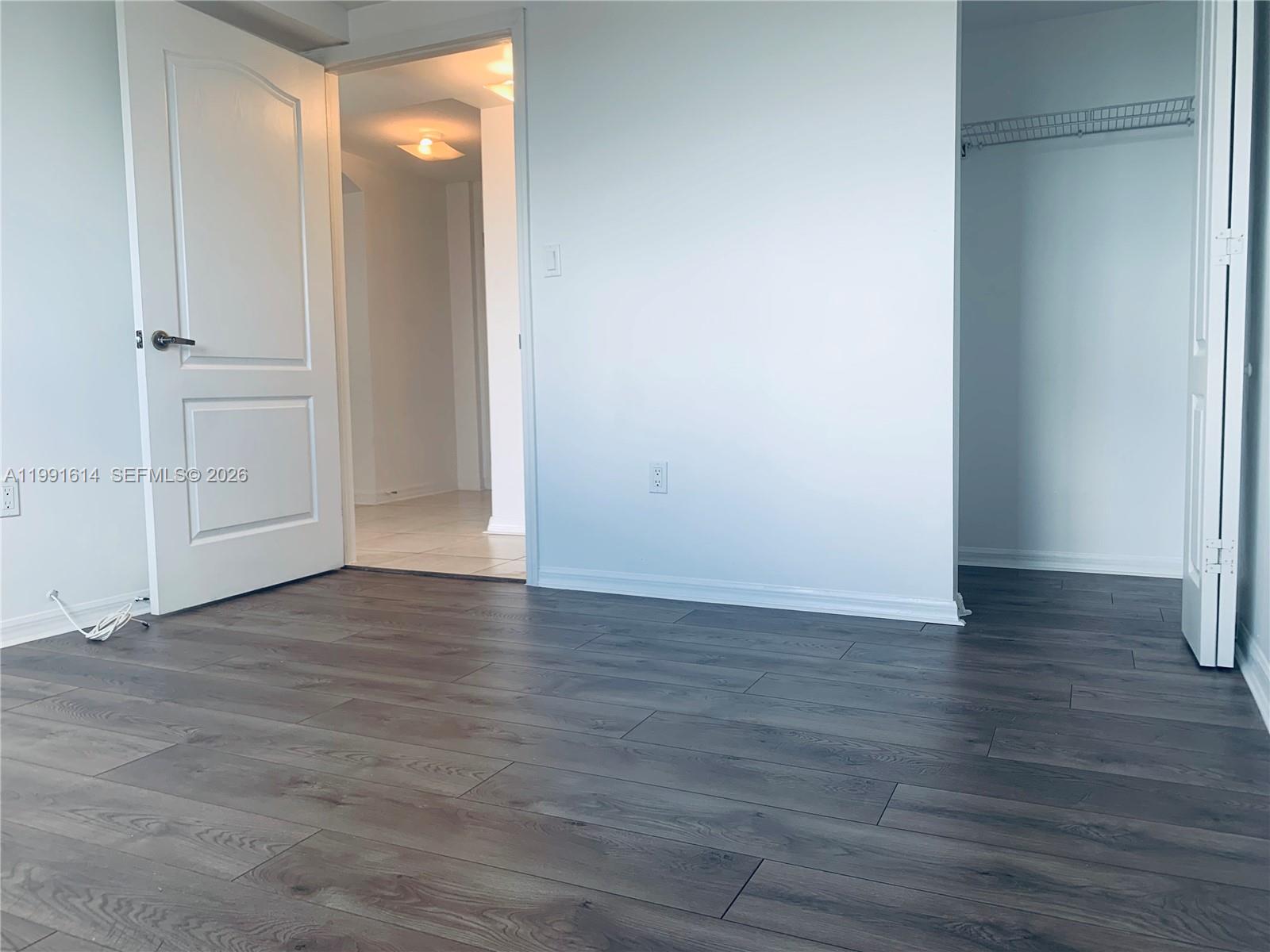 An empty room features dark wood-look flooring, a white door, and an open closet — 406 NW 22nd Ave # 702, Miami FL 33125, MIAMI, FL