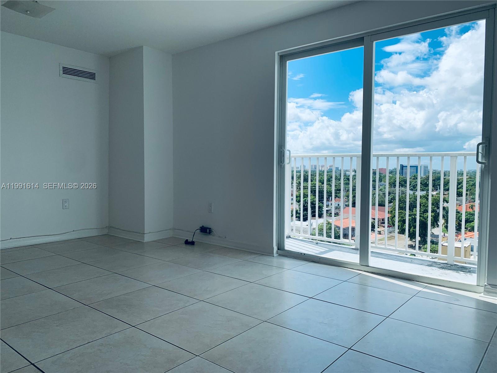 An empty room features white walls, light-colored tile flooring, and a sliding glass balcony door — 406 NW 22nd Ave # 702, Miami FL 33125, MIAMI, FL