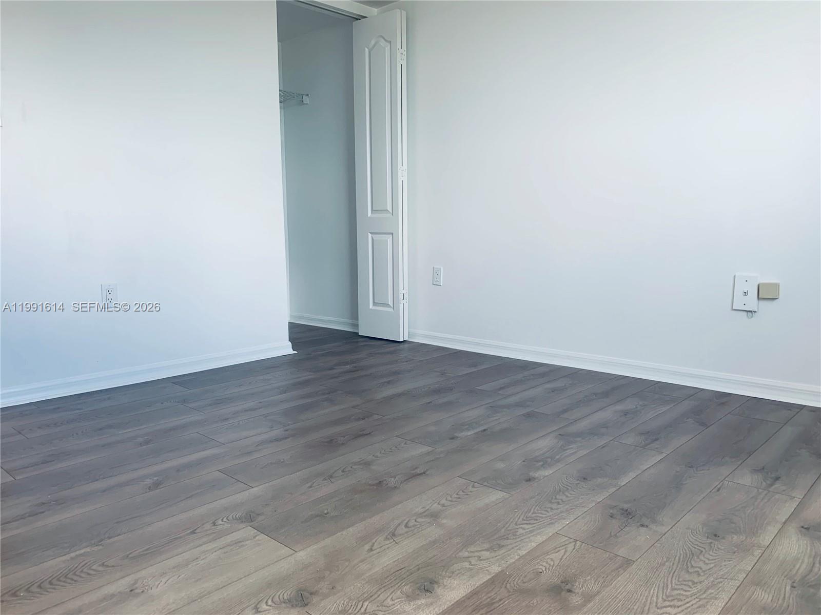 An empty room features white walls, baseboard trim, and dark wood-look laminate flooring — 406 NW 22nd Ave # 702, Miami FL 33125, MIAMI, FL