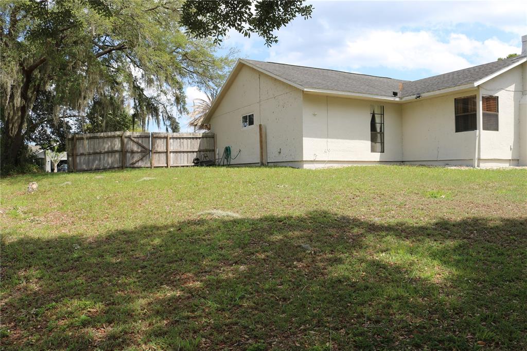 A side view of a beige house with a wooden fence and a grassy yard — 2392 BRIMHALL COURT, DELTONA, FL