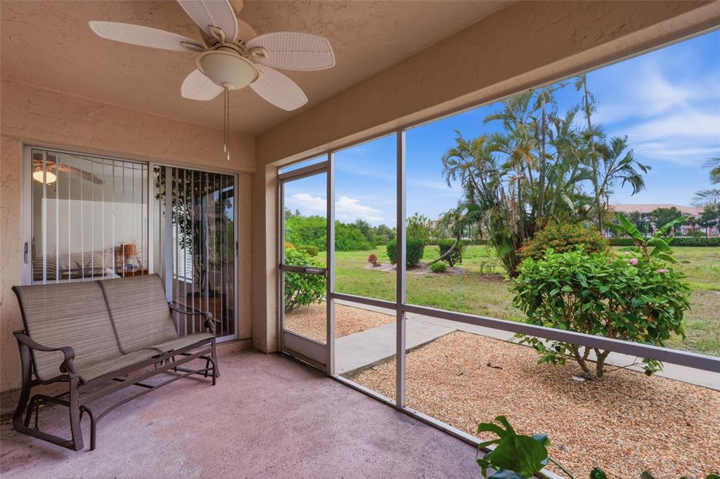 A screened-in patio features a ceiling fan, a metal bench, and a view of landscaping — 16211 DUBLIN CIRCLE UNIT 104, FORT MYERS, FL