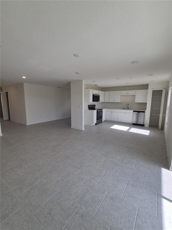 An open-concept kitchen with white cabinets and tile flooring flows into a large living area — 3016 CASCADE CIRCLE, LAKE WALES, FL