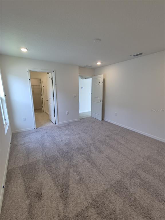 A bedroom with beige carpet, white walls, recessed lighting, and two open doorways — 3016 CASCADE CIRCLE, LAKE WALES, FL
