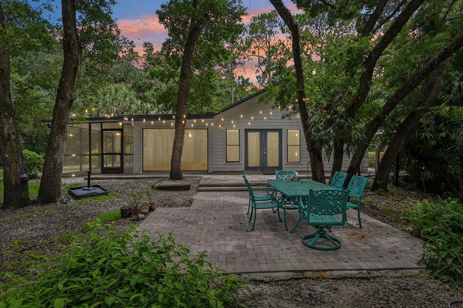 A patio with a metal dining set sits in front of a house with string lights — 16700 96th Terrace N, Jupiter FL 33478, JUPITER, FL
