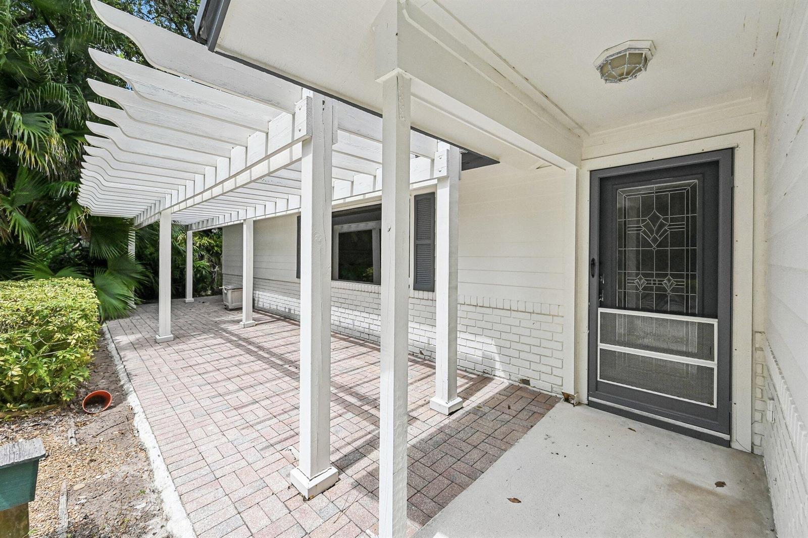 A white pergola covers a brick patio area leading to a dark gray front door — 16700 96th Terrace N, Jupiter FL 33478, JUPITER, FL