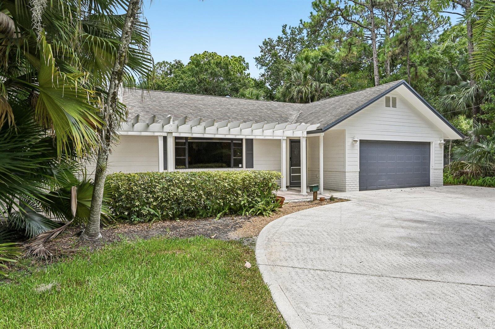A single-story house with a white exterior, a gray garage door, and a wooden pergola — 16700 96th Terrace N, Jupiter FL 33478, JUPITER, FL