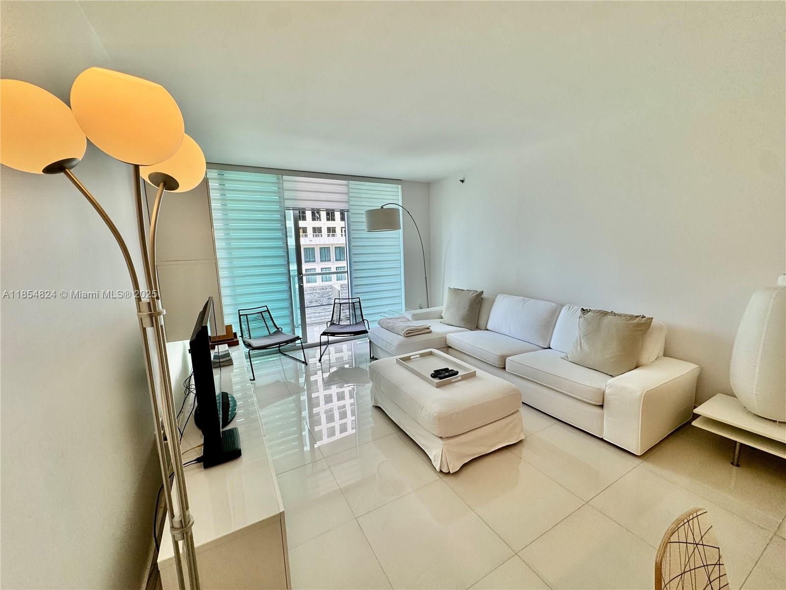 A bright living room features a white sectional sofa, matching ottoman, and glossy tiled floors — 500 Brickell Ave # 1204, Miami FL 33131, MIAMI, FL