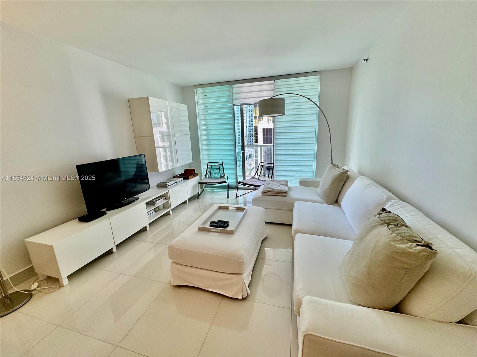 A modern living room features white furniture, a sectional sofa, and large floor-to-ceiling windows — 500 Brickell Ave # 1204, Miami FL 33131, MIAMI, FL