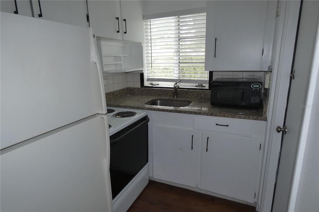 A small kitchen features white cabinets, a white stove, a granite countertop, and a sink — 2567 15TH AVENUE N UNIT 2, ST PETERSBURG, FL