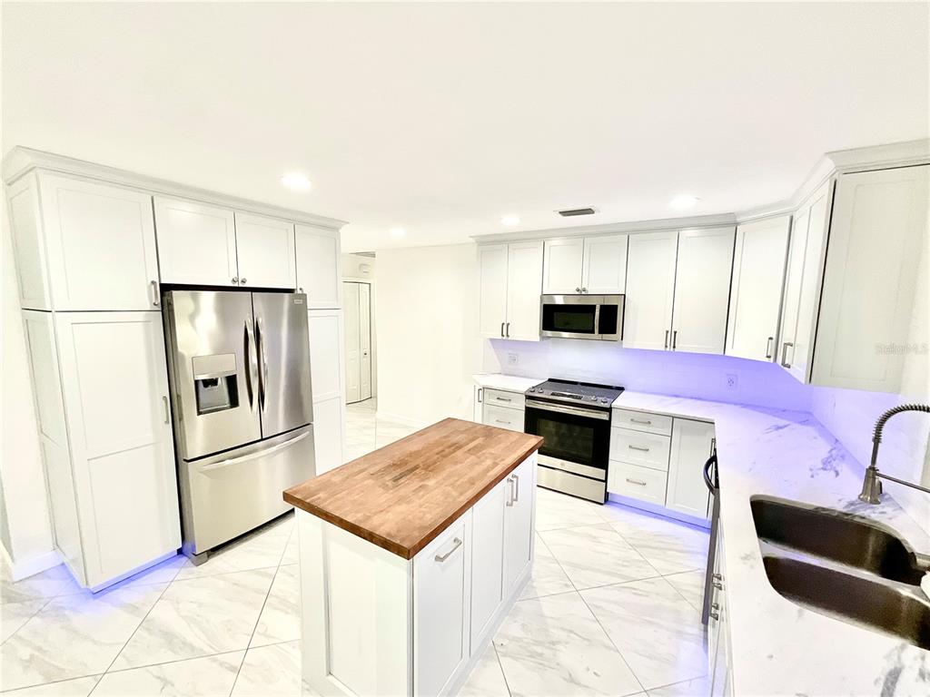 A modern kitchen features white cabinetry, stainless steel appliances, a wood-topped island, and marble flooring — 1545 INDIANA AVENUE, PALM HARBOR, FL