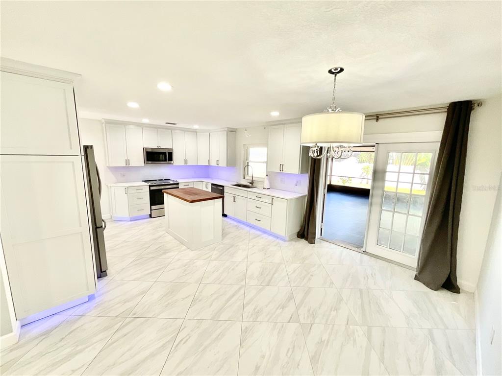 A white kitchen with a wood-topped island, marble-look tile floors, and under-cabinet purple lighting — 1545 INDIANA AVENUE, PALM HARBOR, FL