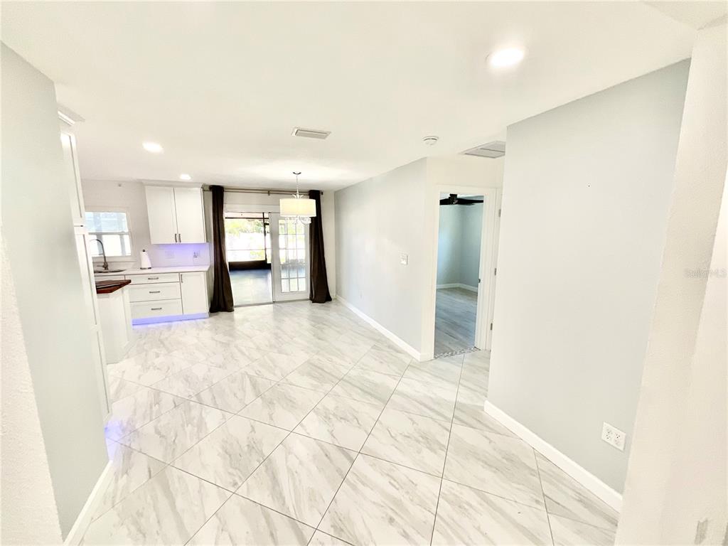 An open-concept kitchen and dining area features white cabinets, marble-look tile flooring, and sliding doors — 1545 INDIANA AVENUE, PALM HARBOR, FL