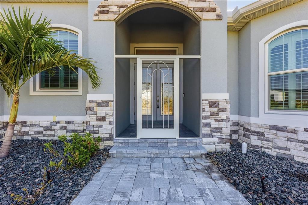 The exterior of a house features a stone-accented entryway with a screened door and walkway — 8314 TRACY CIRCLE, PORT CHARLOTTE, FL