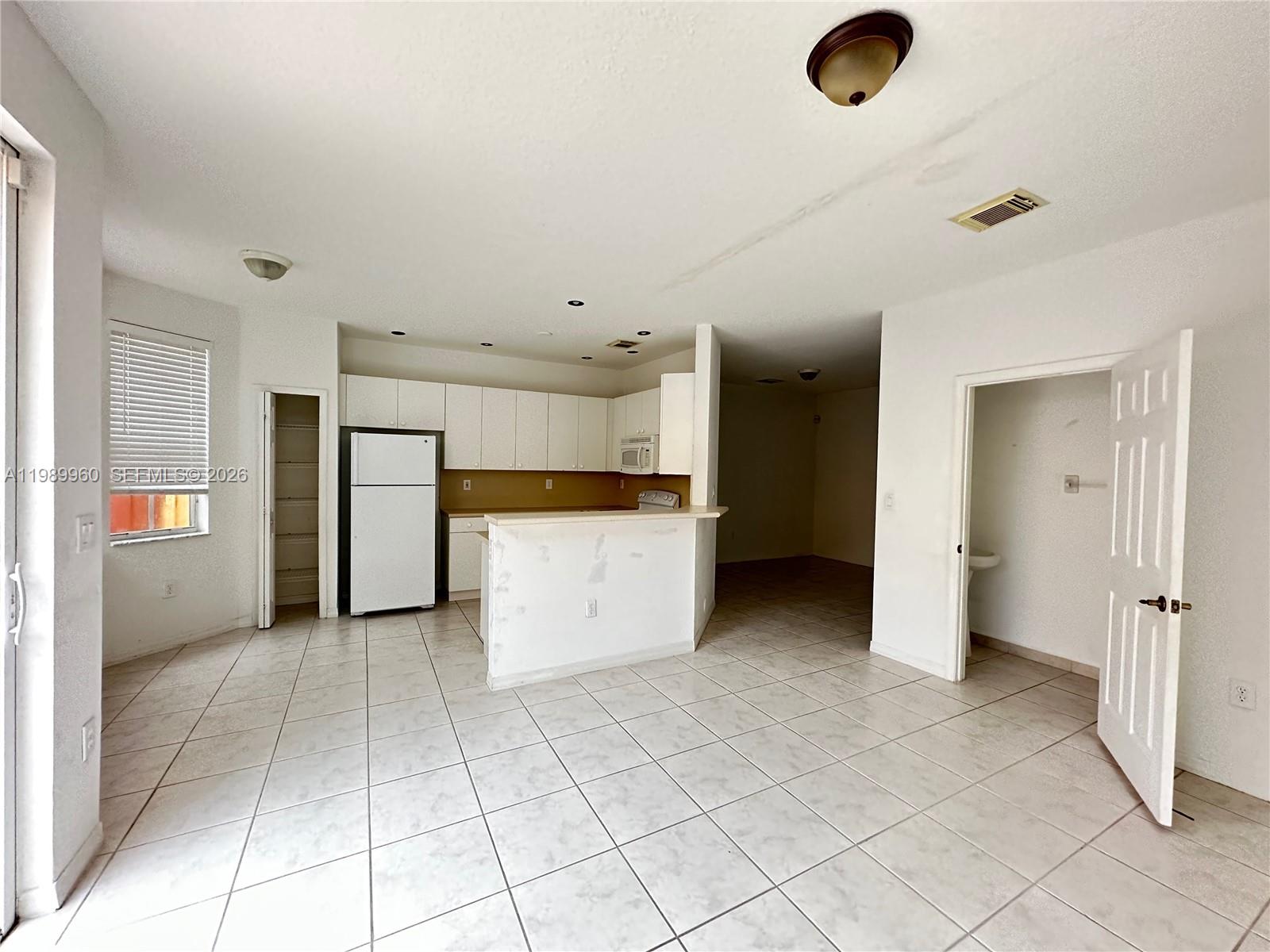 An open-concept kitchen with white cabinets and tile flooring connects to an adjacent living area — 16602 SW 78th Ter, Miami FL 33193, MIAMI, FL