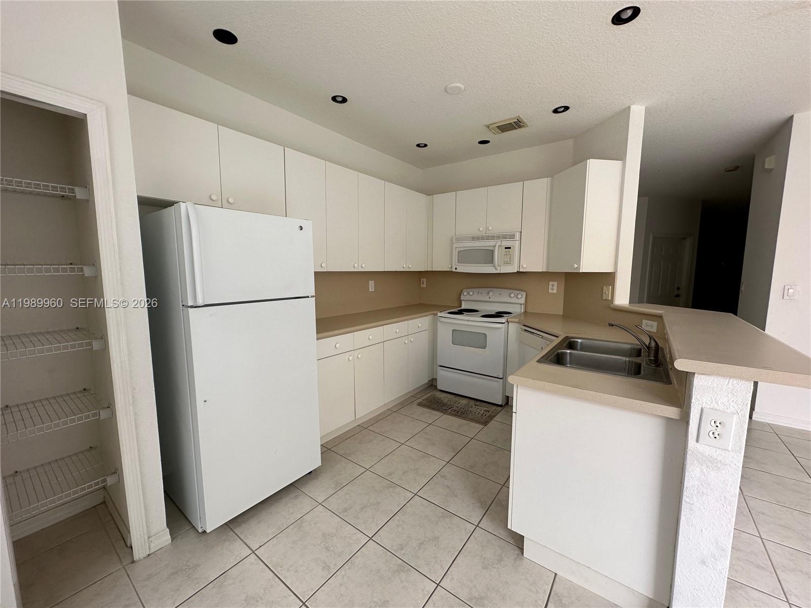 A kitchen features white cabinetry, white appliances, a double sink, and tiled flooring — 16602 SW 78th Ter, Miami FL 33193, MIAMI, FL