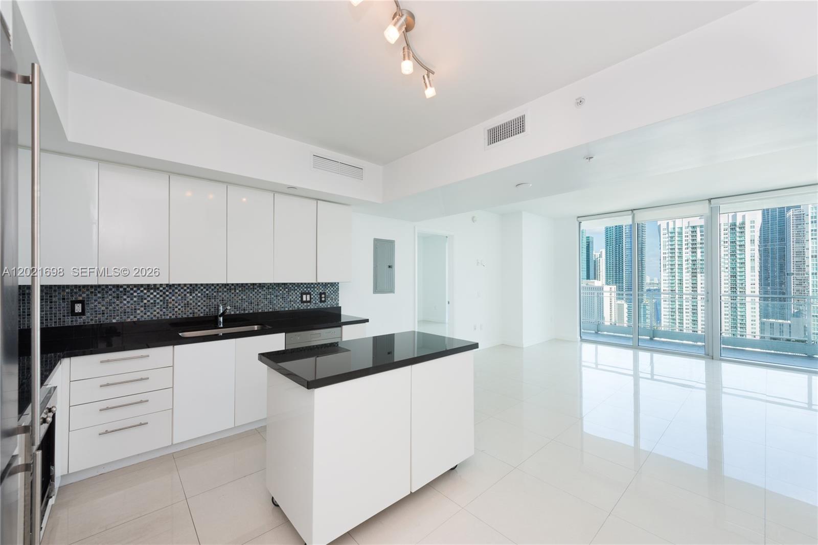 A modern kitchen with white cabinets, black countertops, and a rolling island overlooks city skyscrapers — 92 SW 3rd Street # 2812, Miami FL 33130, MIAMI, FL