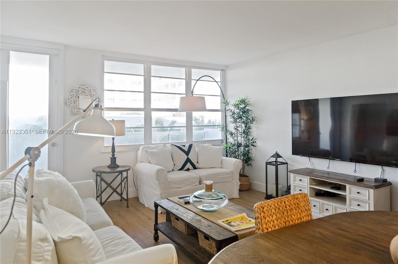 A bright living room features white sofas, a wooden coffee table, and a wall-mounted television — 100 Lincoln Rd # 410, Miami Beach FL 33139, MIAMI BEACH, FL