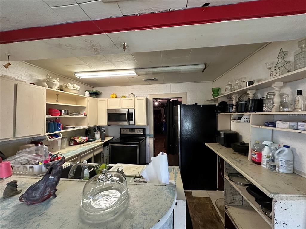 A kitchen features white cabinets, open shelving, a black refrigerator, and a stove — 1105 NE 1ST STREET, MULBERRY, FL