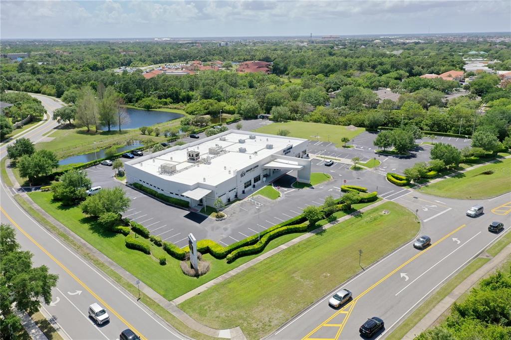 An aerial view shows a commercial building with a parking lot surrounded by green landscaping — 7965 SPYGLASS HILL ROAD, VIERA, FL