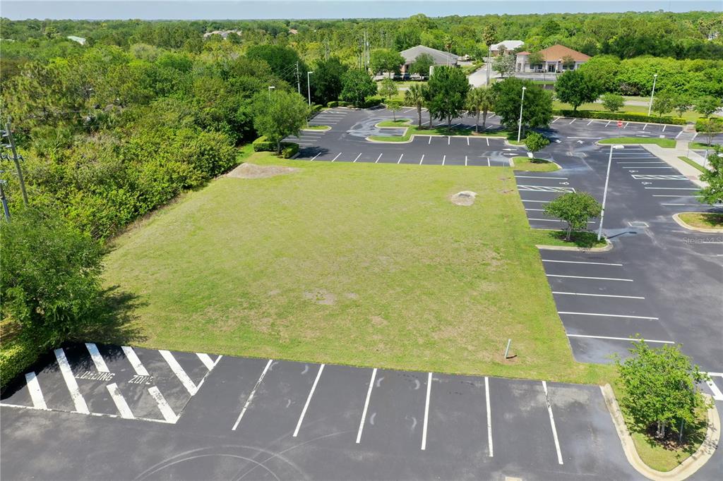 An aerial view shows a vacant grassy lot surrounded by a paved parking area — 7965 SPYGLASS HILL ROAD, VIERA, FL