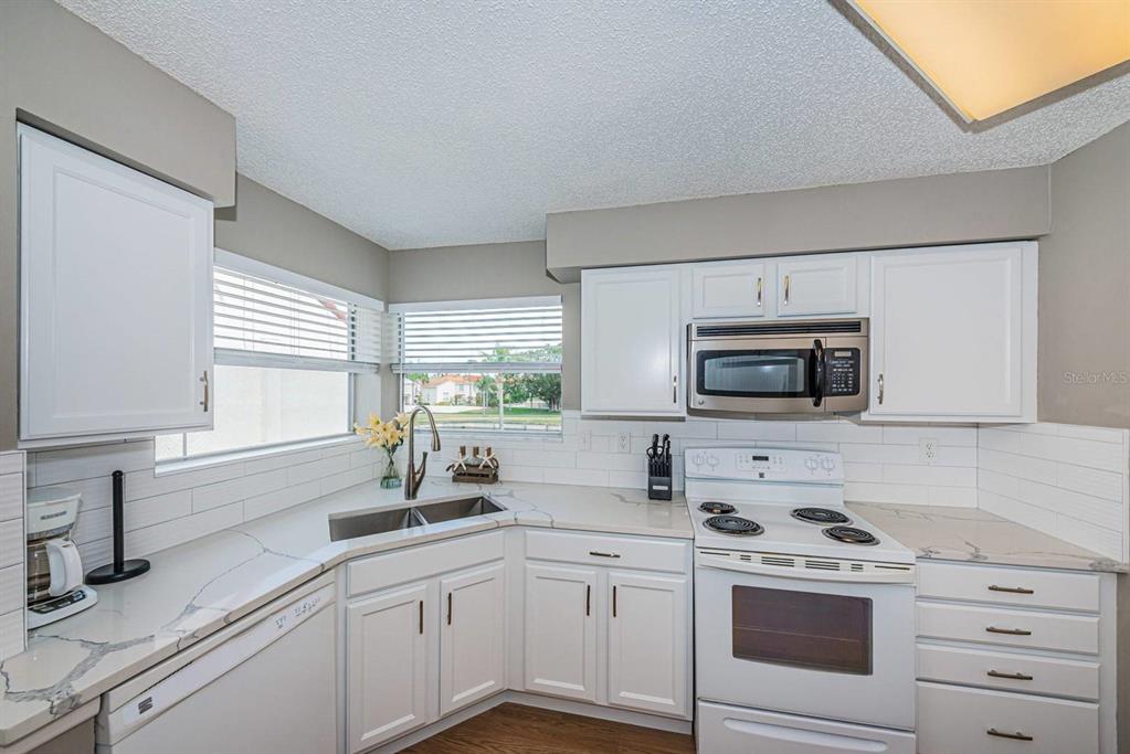 A kitchen features white cabinets, stainless steel appliances, a corner sink, and marble-look countertops — 6077 BAHIA DEL MAR BOULEVARD UNIT 221, ST PETERSBURG, FL