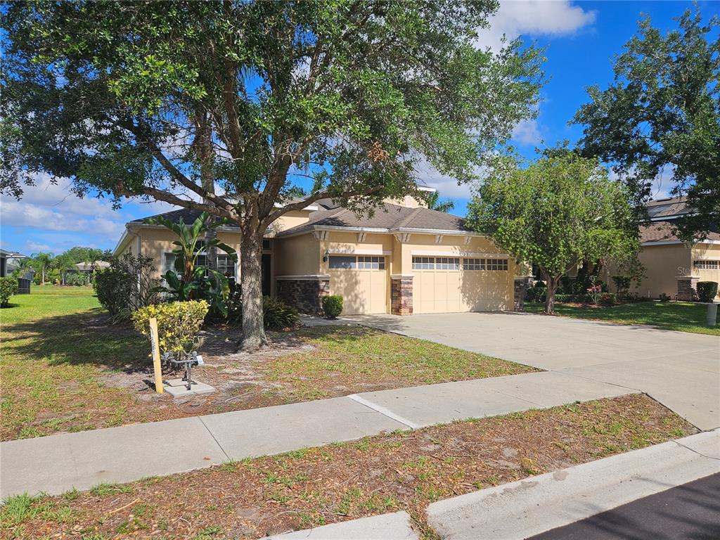 A single-story house with a two-car garage, stone accents, and a large tree in front — 118 PEONY COURT, BRADENTON, FL