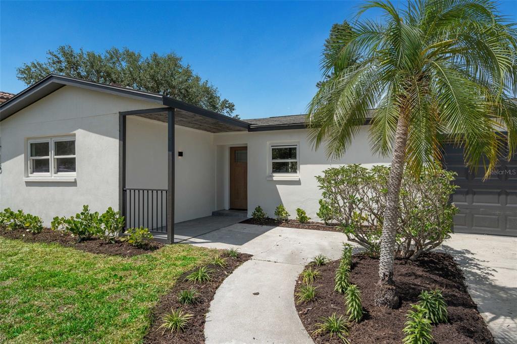 A single-story house with a white stucco exterior, a covered entryway, and a palm tree — 1715 DELAWARE AVENUE NE, ST PETERSBURG, FL