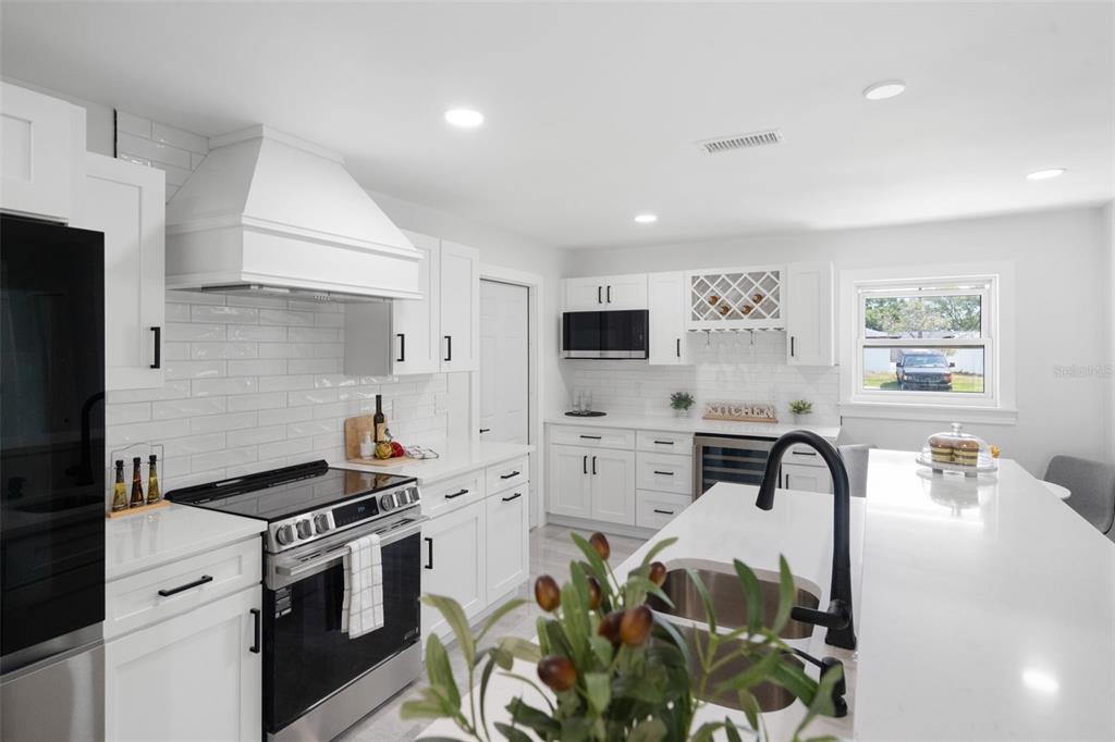 A modern white kitchen features a large island, stainless steel appliances, and subway tile backsplash — 1715 DELAWARE AVENUE NE, ST PETERSBURG, FL